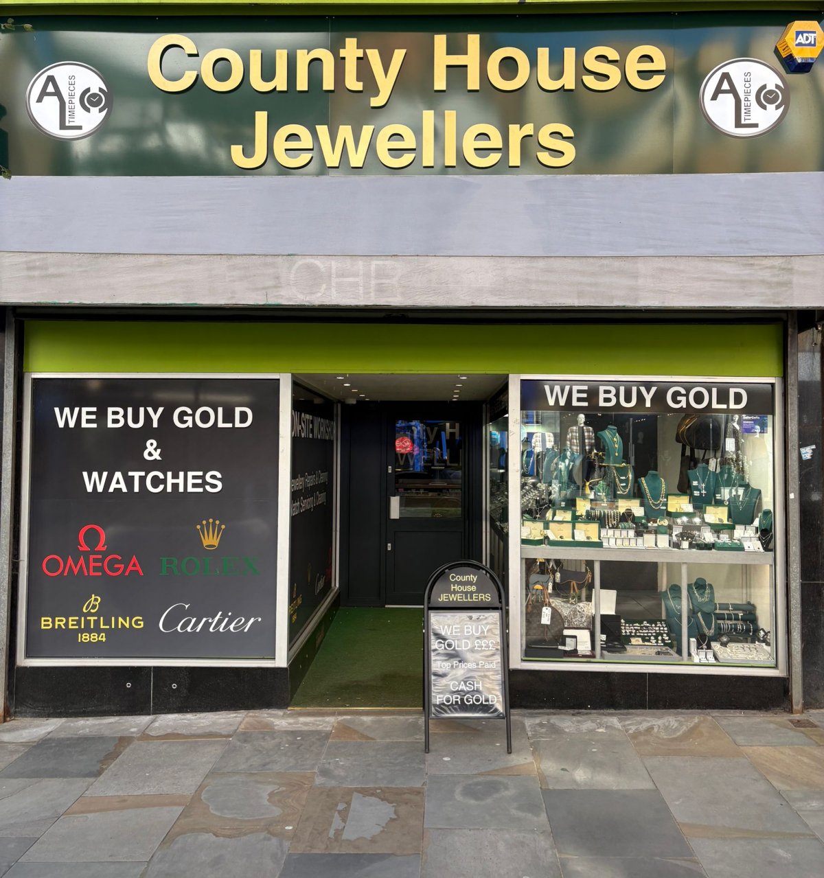Front view of County House Jewellers shop with signage “We Buy Gold & Watches,” featuring Omega, Rolex, Breitling, and Cartier.